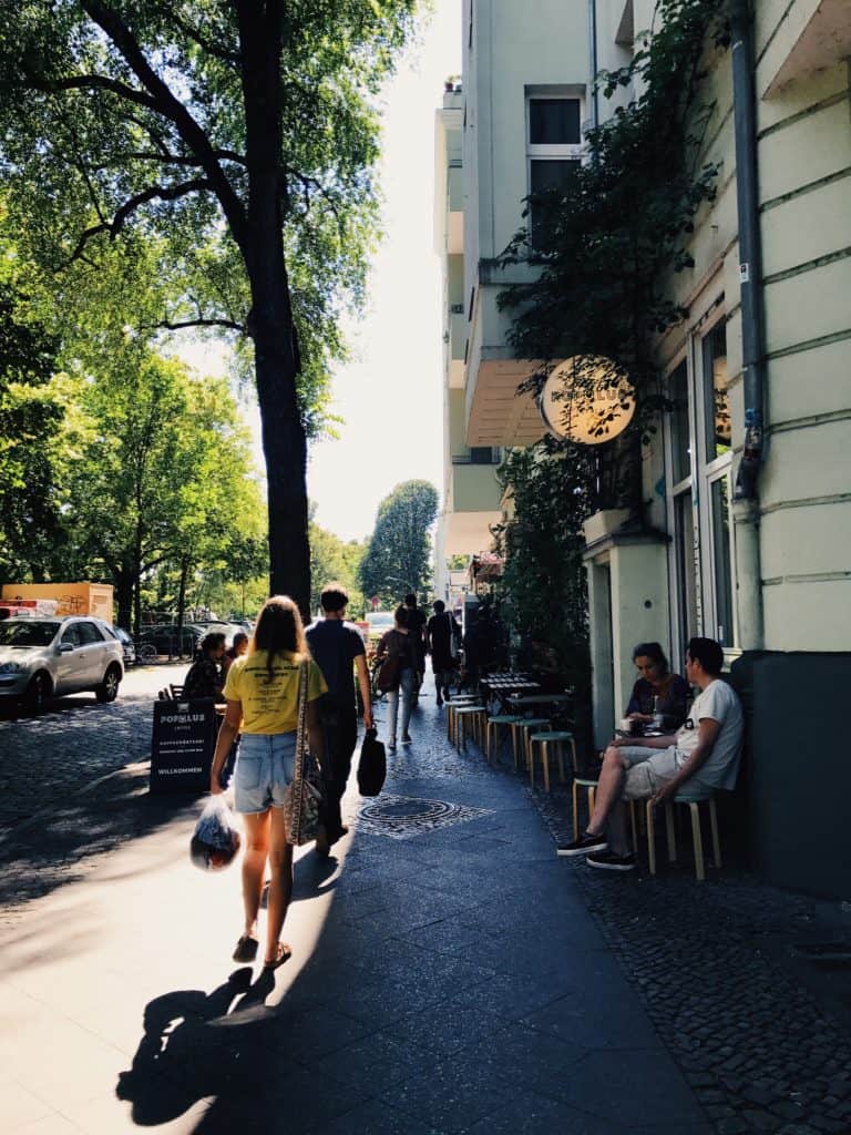People walking and sitting outside, on the sidewalk past Populus Cafe in Berlin.
